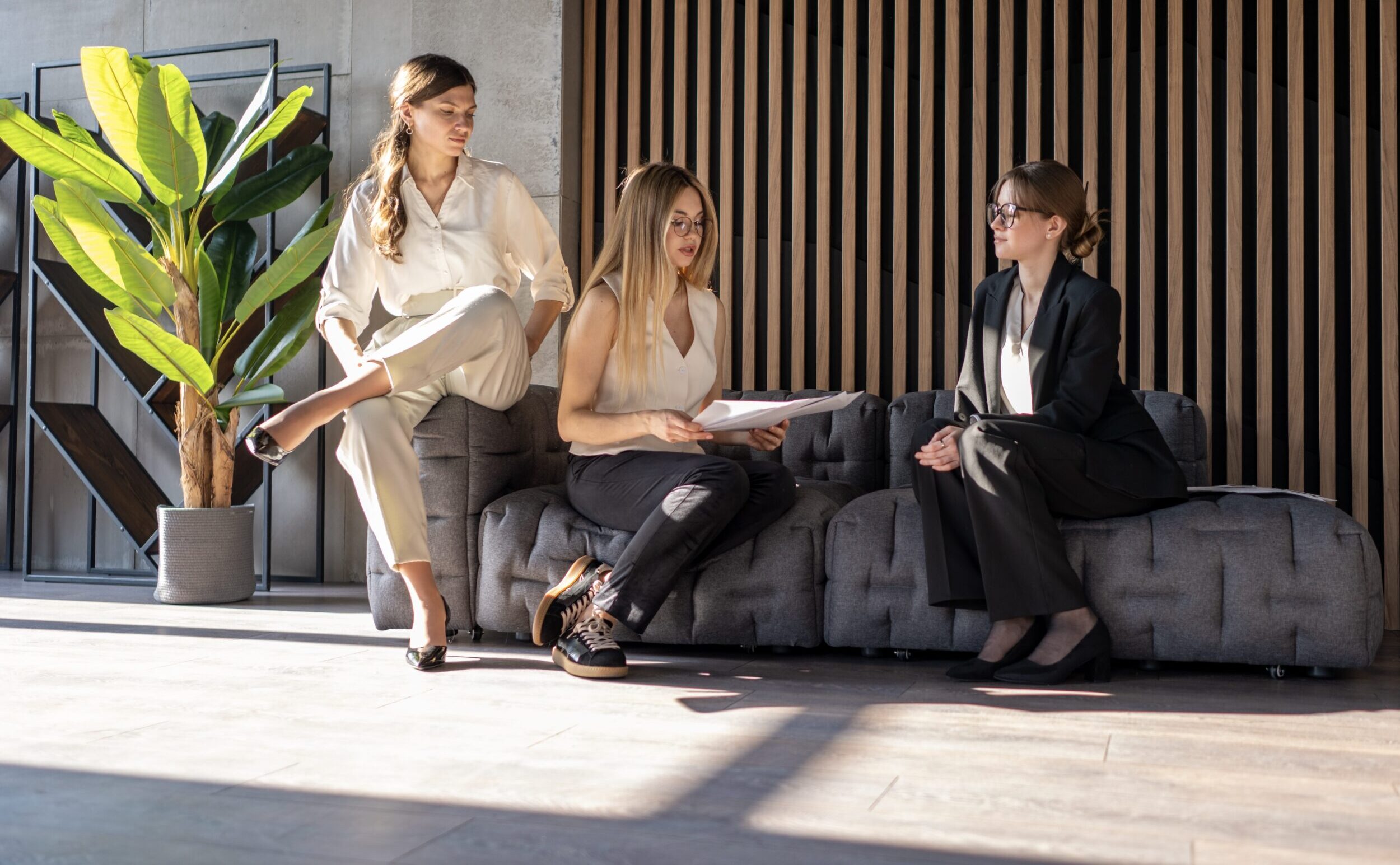 Three women in business attire having a discussion in a modern office setting.