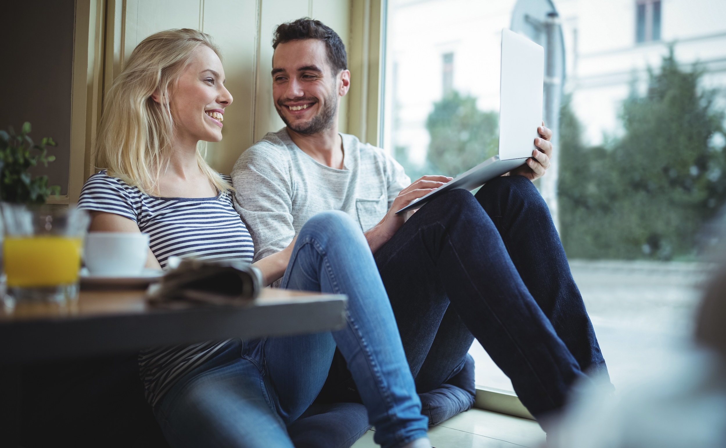 Couple using a laptop in a cafe, smiling and looking at each other