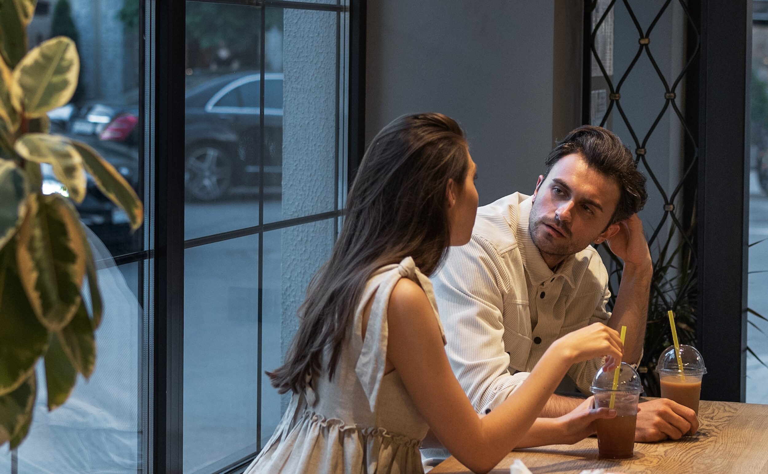 Couple in cafe, man looking bored during date with woman holding iced coffee.
