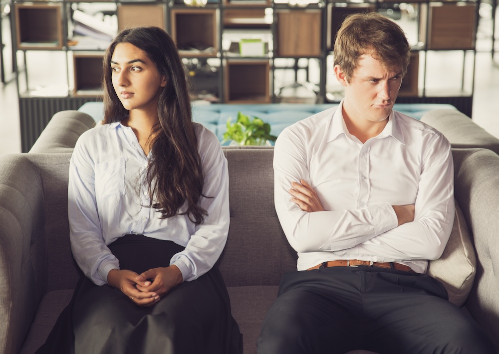 Couple sitting apart on a couch, looking upset and disconnected